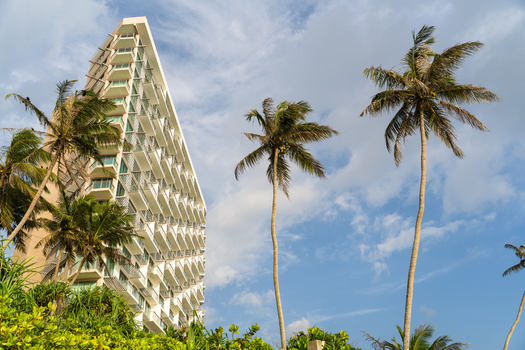 View of a modern high rise hotel building with numerous balconies rising above tall palm trees and lush tropical greenery under a blue sky in Galle Southern Province Sri Lanka.