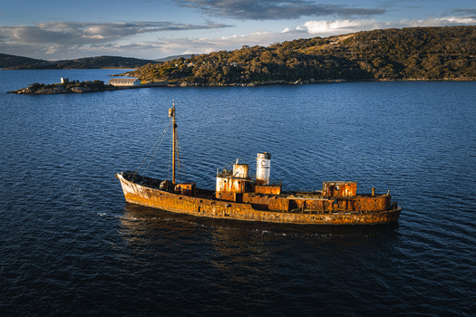 Aerial view of the rusty shipwreck Cheynes II anchored in the calm blue waters of the bay near the historic buildings of Camp Quaranup on the Vancouver Peninsula Western Australia Australia. Aerial view of the rusty shipwreck Cheynes II anchored in the calm blue waters of the bay near the historic buildings of Camp Quaranup on the Vancouver Peninsula Western Australia Australia.