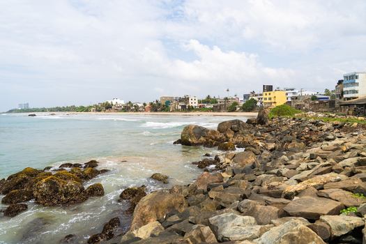 View of the rocky coastline and sandy beach with coastal buildings under a cloudy sky in Galle Southern Province Sri Lanka.