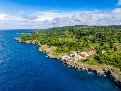 Aerial view of the rugged coastline with lush green vegetation rocky cliffs and coastal villas overlooking the deep blue sea in Rio San Juan Maria Trinidad Sanchez Dominican Republic. Aerial view of the rugged coastline with lush green vegetation rocky cliffs and coastal villas overlooking the deep blue sea in Rio San Juan Maria Trinidad Sanchez Dominican Republic.