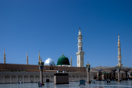 View of Al Masjid e Nabawi with its iconic green dome and tall minarets under a clear blue sky in the courtyard of the Prophet s Mosque in Madinah Al Madinah Province Saudi Arabia.