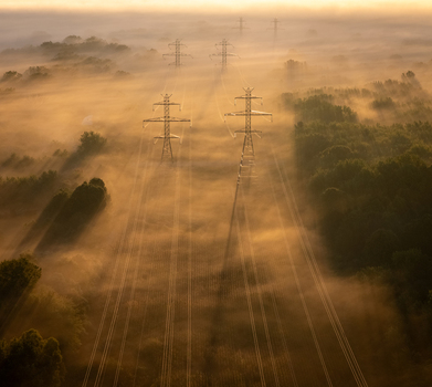 Aerial view of transmission lines and towers rising above a dense layer of morning fog with golden sunlight casting long shadows over the landscape in Bridgman Michigan United States.