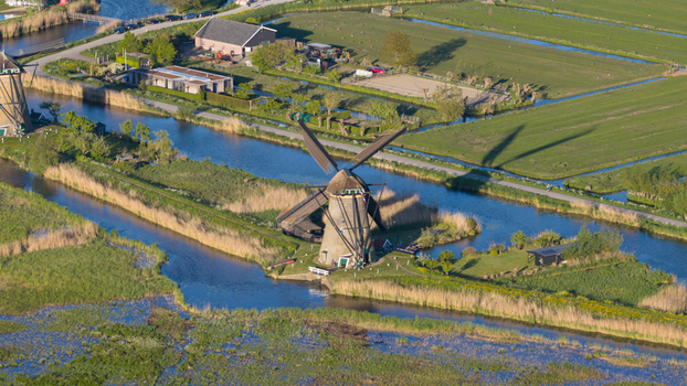 Aerial view of the historic windmills and water canals surrounded by lush green fields and reeds under bright sunlight Kinderdijk South Holland Netherlands. Aerial view of the historic windmills and water canals surrounded by lush green fields and reeds under bright sunlight Kinderdijk South Holland Netherlands.