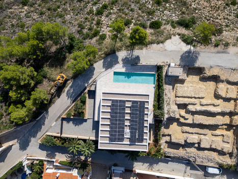 Aerial view of a modern house with solar panels on the roof and a turquoise swimming pool situated near an archaeological excavation site and pine trees in Moraira Valencian Community Spain.