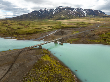 Aerial view of Kerlingarfjoll featuring a bridge crossing a turquoise glacial river with snow capped mountains in the background in Hrunamannahreppur Iceland. Aerial view of Kerlingarfjoll featuring a bridge crossing a turquoise glacial river with snow capped mountains in the background in Hrunamannahreppur Iceland.