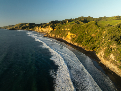 Aerial view of the dramatic Waikawau coastline where dark sands meet the crashing waves and green hills under the clear sky Waikawau Waikato Region New Zealand. Aerial view of the dramatic Waikawau coastline where dark sands meet the crashing waves and green hills under the clear sky Waikawau Waikato Region New Zealand.