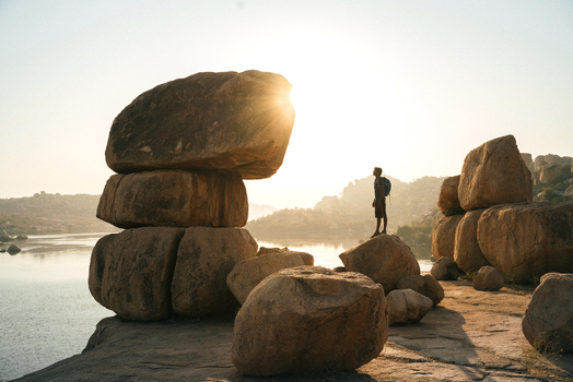 View of a hiker standing on a large boulder overlooking the Tungabhadra River at sunset in Hampi Karnataka India. View of a hiker standing on a large boulder overlooking the Tungabhadra River at sunset in Hampi Karnataka India.