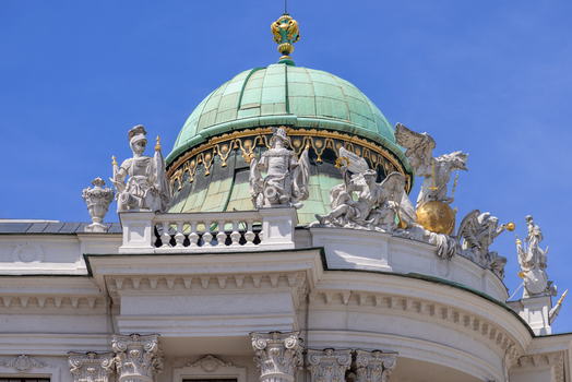 View of the ornate green copper dome and intricate stone sculptures of the historic Hofburg palace against a clear blue sky in Vienna Vienna Austria.