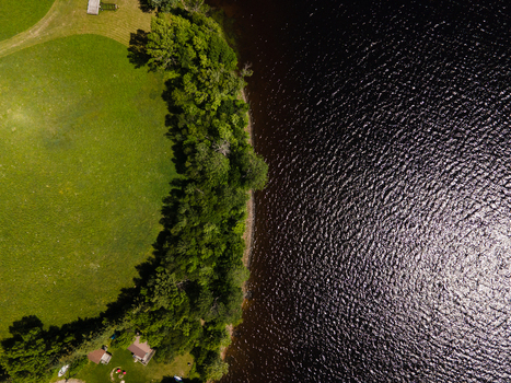 Aerial view of the shoreline of Commanda Lake with lush green trees bordering a grassy lawn and dark rippling water in Restoule Ontario Canada. Aerial view of the shoreline of Commanda Lake with lush green trees bordering a grassy lawn and dark rippling water in Restoule Ontario Canada.