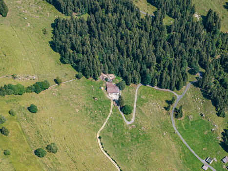 Aerial view of a mountain chalet nestled in the green pastures of Justistal near Niederhorn with winding roads and dense pine forests in the Bernese Alps Sigriswil Bern Switzerland. Aerial view of a mountain chalet nestled in the green pastures of Justistal near Niederhorn with winding roads and dense pine forests in the Bernese Alps Sigriswil Bern Switzerland.