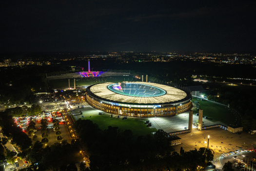 Berlin Germany 26 September 2026 Aerial view of Olympiastadion Berlin illuminated at night showcasing its iconic architecture surrounding parkland and parking areas under a dark sky.