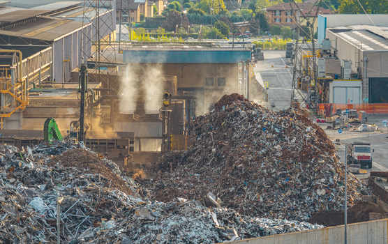 Aerial view of large piles of scrap metal awaiting processing inside the steel manufacturing complex with industrial machinery and steam rising in Brescia Lombardy Italy. Aerial view of large piles of scrap metal awaiting processing inside the steel manufacturing complex with industrial machinery and steam rising in Brescia Lombardy Italy.