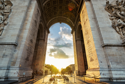 View of the Arc de Triomphe looking through the massive stone archway at sunset with people gathered at the base and intricate carvings on the walls Paris Ile de France France.