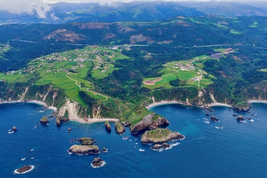 Aerial view of Silence Beach Viewpoint with its rugged coastline green meadows steep cliffs and rocky islets in the blue Cantabrian Sea in Cudillero Asturias Spain.