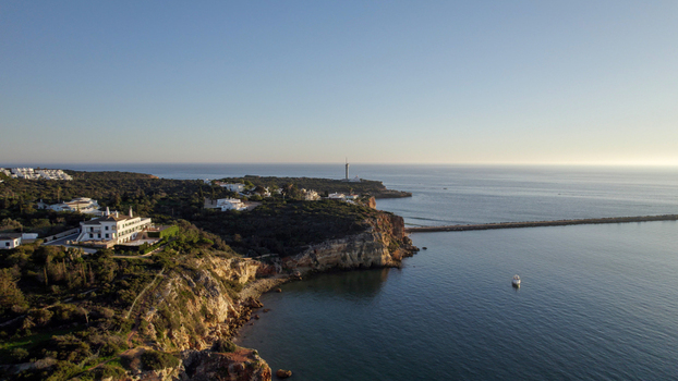 Aerial view of the Ferragudo coastline featuring rugged cliffs a white lighthouse on the headland calm blue sea and coastal villas in Ferragudo Faro District Portugal.