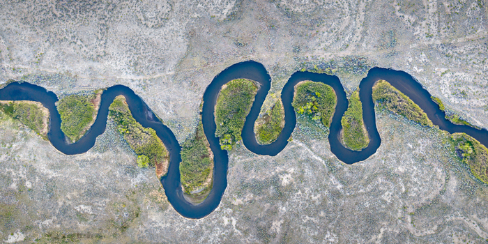 Aerial view of the meandering Owens River flowing through an arid landscape with lush green vegetation along the banks in Inyo County California United States.