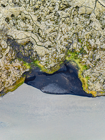 Aerial view of rugged volcanic lava fields meeting the dark waters of the coast with mossy patches and textured rock formations in Iceland. Aerial view of rugged volcanic lava fields meeting the dark waters of the coast with mossy patches and textured rock formations in Iceland.