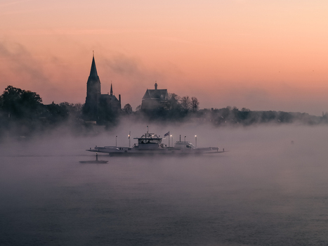 Aerial view of a ferry boat crossing the misty Meuse river with the historic church spire of Kessel silhouetted against a soft sunrise sky Kessel Limburg Netherlands.