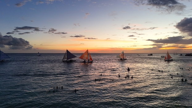 Malay Philippines 02 May 2026 Aerial view of Boracay Island with traditional paraw sailboats sailing on the calm sea during a vibrant sunset with people swimming in the water.