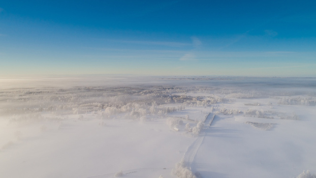 Aerial view of a vast snow covered landscape blanketed in thick morning fog with frost covered trees and a clear blue sky LATVIA. Aerial view of a vast snow covered landscape blanketed in thick morning fog with frost covered trees and a clear blue sky LATVIA.