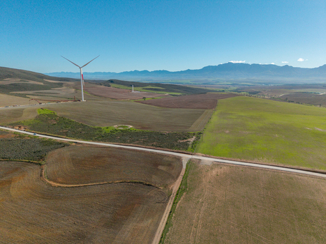 Aerial view of a large wind turbine standing in vast agricultural fields under a clear blue sky with distant mountains Swellendam Western Cape South Africa. Aerial view of a large wind turbine standing in vast agricultural fields under a clear blue sky with distant mountains Swellendam Western Cape South Africa.