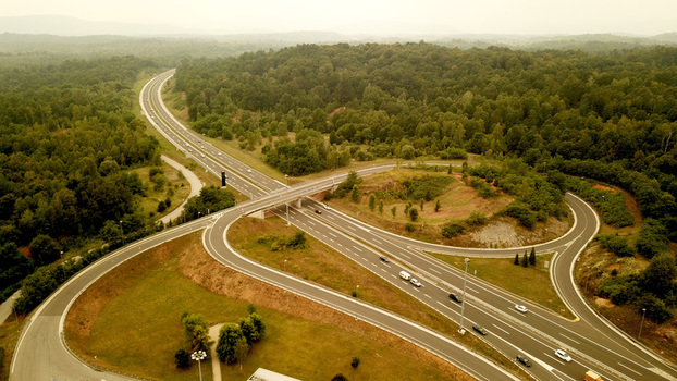 Aerial view of a highway interchange surrounded by dense green forests with cars driving on the asphalt roads in Croatia.