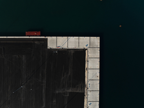 Aerial view of a geometric concrete pier corner meeting dark water with a small red container in Augusta Sicily Italy. Aerial view of a geometric concrete pier corner meeting dark water with a small red container in Augusta Sicily Italy.