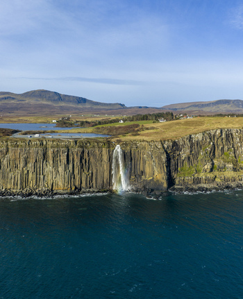Aerial view of Mealt Falls cascading down the basalt columns of Kilt Rock into the sea under a clear blue sky in Isle of Skye Scotland United Kingdom. Aerial view of Mealt Falls cascading down the basalt columns of Kilt Rock into the sea under a clear blue sky in Isle of Skye Scotland United Kingdom.