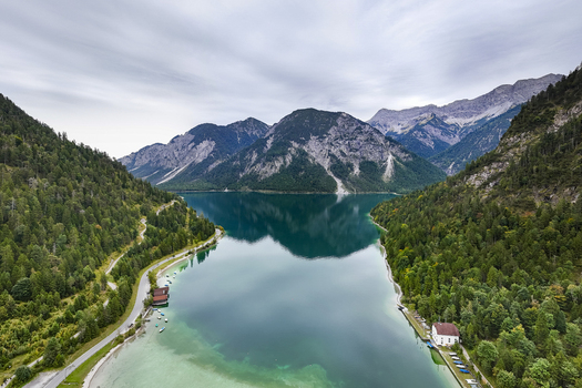 Aerial view of a serene lake reflecting the towering mountains embraced by verdant forests and quaint buildings Plansee Tyrol Austria. Aerial view of a serene lake reflecting the towering mountains embraced by verdant forests and quaint buildings Plansee Tyrol Austria.