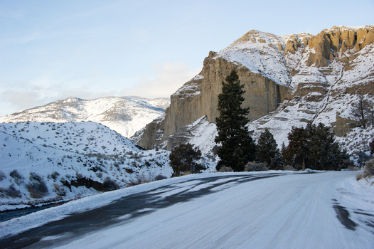 View of a snow covered road winding through the rugged snow capped mountains and evergreen trees of Yellowstone National Park United States.