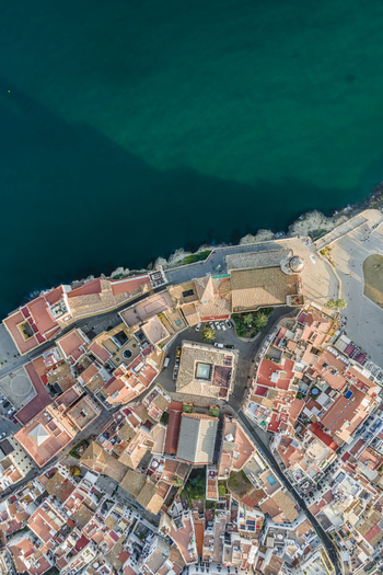 Aerial view of the historic center with terracotta rooftops the Church of Sant Bartomeu i Santa Tecla and the deep blue Mediterranean Sea Sitges Catalonia Spain. Aerial view of the historic center with terracotta rooftops the Church of Sant Bartomeu i Santa Tecla and the deep blue Mediterranean Sea Sitges Catalonia Spain.