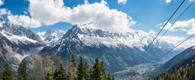 View of the Mer de Glace panorama in the Alps with snow capped mountain peaks lush pine forests and a clear blue sky Chamonix Auvergne Rhone Alpes France.