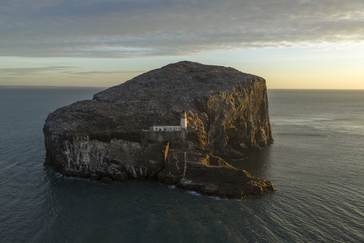 Aerial view of Bass Rock Lighthouse perched on the steep cliffs of a volcanic island surrounded by the calm sea during golden hour North Berwick Scotland United Kingdom. Aerial view of Bass Rock Lighthouse perched on the steep cliffs of a volcanic island surrounded by the calm sea during golden hour North Berwick Scotland United Kingdom.