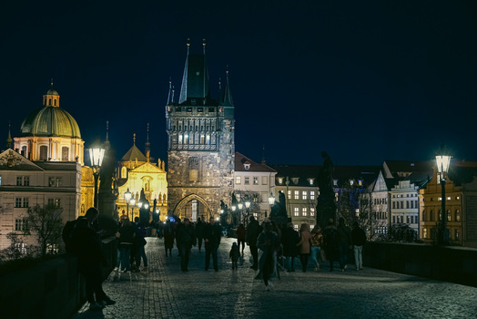Prague Prague Czechia 03 November 2021 View of Charles Bridge at night with historic stone towers illuminated street lamps and people walking along the cobblestone path. Prague Prague Czechia 03 November 2021 View of Charles Bridge at night with historic stone towers illuminated street lamps and people walking along the cobblestone path.