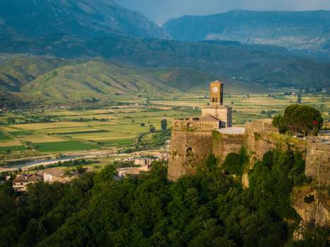Aerial view of the historic Gjirokaster Fortress and its clock tower overlooking the green Drino Valley and surrounding mountains Gjirokaster Gjirokaster County Albania. Aerial view of the historic Gjirokaster Fortress and its clock tower overlooking the green Drino Valley and surrounding mountains Gjirokaster Gjirokaster County Albania.
