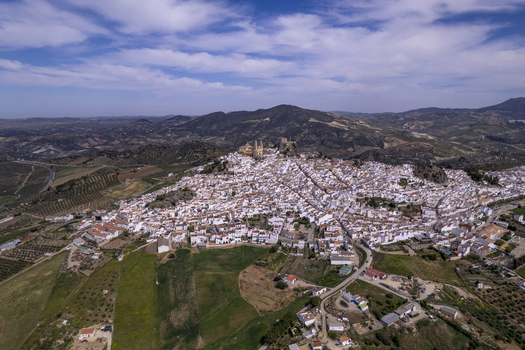 Aerial view of the white village of Olvera perched on a hill with its historic church and castle surrounded by olive groves and rolling hills in Olvera Andalusia Spain. Aerial view of the white village of Olvera perched on a hill with its historic church and castle surrounded by olive groves and rolling hills in Olvera Andalusia Spain.