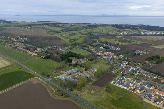 Aerial view of Dirleton Castle and Gardens surrounded by historic stone ruins lush green lawns and the village houses with the sea in the distance Dirleton Scotland United Kingdom. Aerial view of Dirleton Castle and Gardens surrounded by historic stone ruins lush green lawns and the village houses with the sea in the distance Dirleton Scotland United Kingdom.