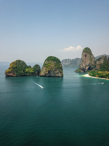 Aerial view of tiny speed boats exploring the giant limestone cliffs and islands in the turquoise blue sea a tropical paradise Phra Nang Krabi Phuket Thailand.