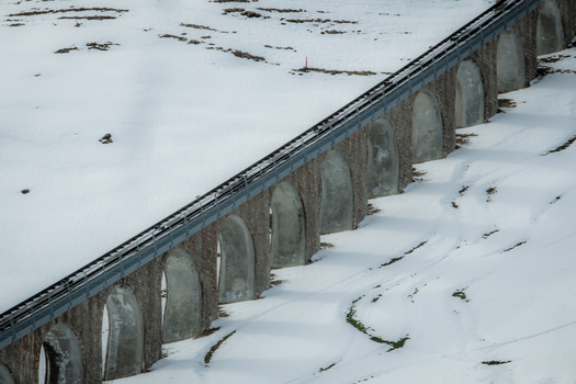 View of a stone railway bridge with arches cutting through a blanket of pristine white snow a stark contrast against the dark tracks Murren Switzerland. View of a stone railway bridge with arches cutting through a blanket of pristine white snow a stark contrast against the dark tracks Murren Switzerland.