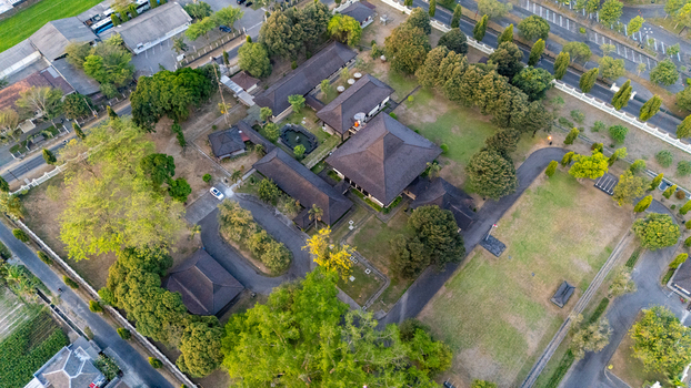 Aerial view of a traditional Indonesian architectural complex featuring dark tiled roofs lush green trees manicured lawns and surrounding roads in Indonesia. Aerial view of a traditional Indonesian architectural complex featuring dark tiled roofs lush green trees manicured lawns and surrounding roads in Indonesia.