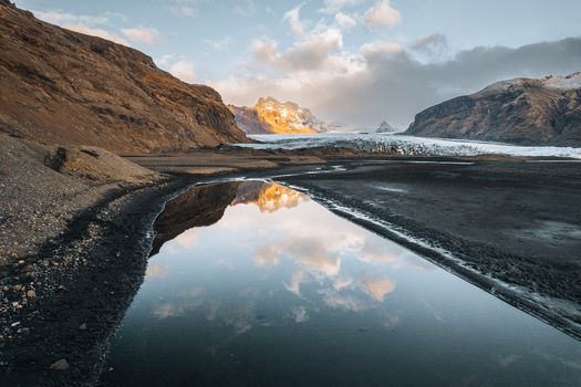 Aerial view of the Skaftafell glacier tongue and rugged mountains reflected in a calm pool of water during golden hour Skaftafell Sveitarfelagid Hornaf Iceland. Aerial view of the Skaftafell glacier tongue and rugged mountains reflected in a calm pool of water during golden hour Skaftafell Sveitarfelagid Hornaf Iceland.