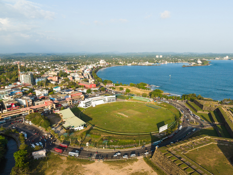 Aerial view of Galle International Stadium and the historic fort walls along the coastline under a clear sky in Galle Southern Province Sri Lanka.