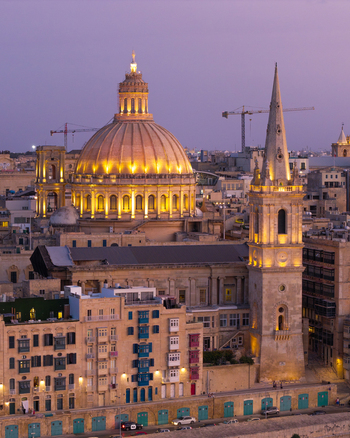Aerial view of the illuminated dome and spire of the Basilica of Our Lady of Mount Carmel rising above the historic limestone buildings of Valletta Port Region Malta. Aerial view of the illuminated dome and spire of the Basilica of Our Lady of Mount Carmel rising above the historic limestone buildings of Valletta Port Region Malta.