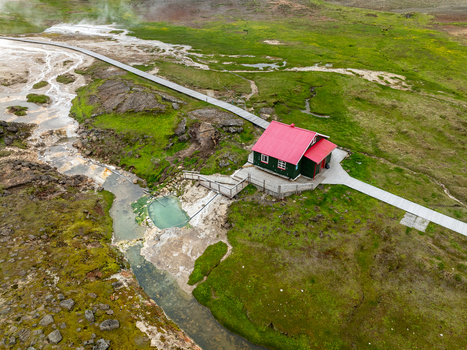 Aerial view of Hveravellir geothermal area featuring a cabin with a red roof wooden walkways and steaming pools in Hunabyggd Iceland.