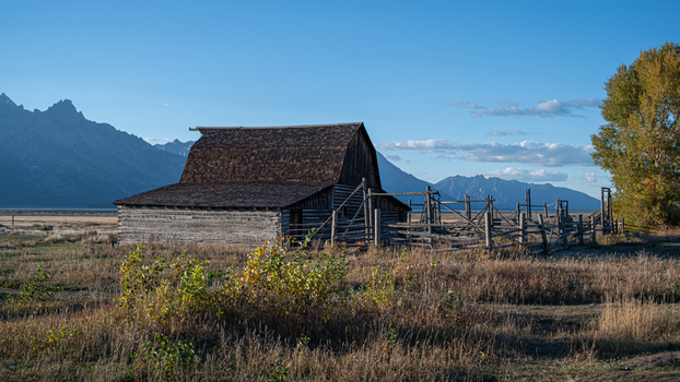 View of the historic wooden barn at Mormon Row in Jackson Hole set against the backdrop of the Teton Range under a clear blue sky in Teton County Wyoming United States.