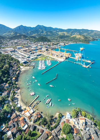 Aerial view of Praia do Machado with shipyard cranes turquoise bay small boats and coastal town buildings in Angra dos Reis Rio de Janeiro Brazil.