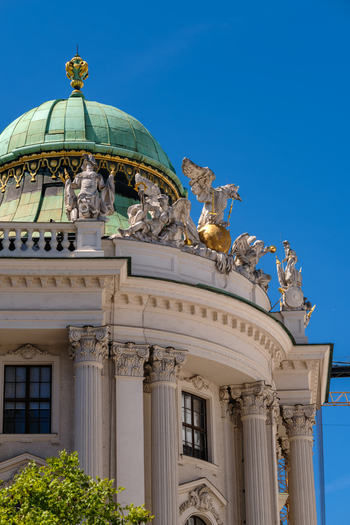 View of the ornate Hofburg Palace featuring its green copper dome white mythological sculptures and Corinthian columns under a clear blue sky in Vienna Vienna Austria. View of the ornate Hofburg Palace featuring its green copper dome white mythological sculptures and Corinthian columns under a clear blue sky in Vienna Vienna Austria.