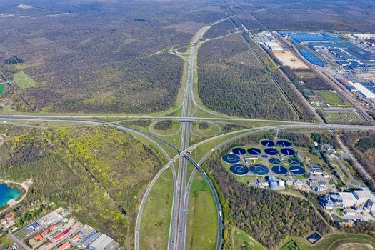 Aerial view of the cloverleaf interchange cuts through the landscape near a water treatment plant contrasting with the surrounding forest Sausheim Grand Est France.