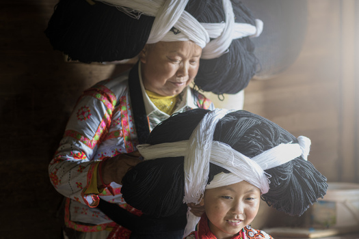 Gaoxing China 29 April 2026 View of a Long Horn Miao woman adjusting the traditional large black and white yarn headdress of a young girl in a wooden interior. Gaoxing China 29 April 2026 View of a Long Horn Miao woman adjusting the traditional large black and white yarn headdress of a young girl in a wooden interior.