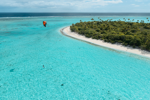 Aerial view of a kite surfer gliding over the turquoise lagoon of Aitutaki with white sand beaches and lush tropical vegetation in the Cook Islands. Aerial view of a kite surfer gliding over the turquoise lagoon of Aitutaki with white sand beaches and lush tropical vegetation in the Cook Islands.